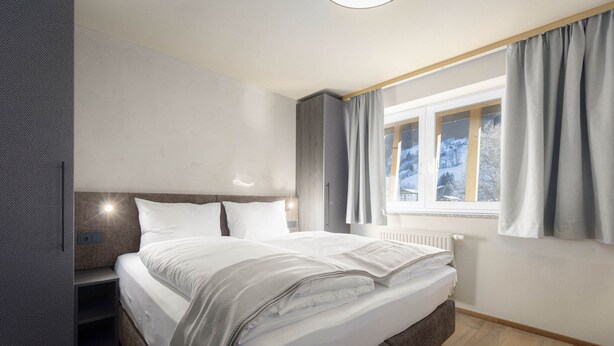 Een moderne slaapkamer met een groot bed, inbouwkasten, een raam met gordijnen en een radiator.