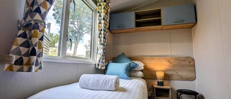 Un dormitorio con cama, mesita de noche, lámpara y ventana con cortinas.