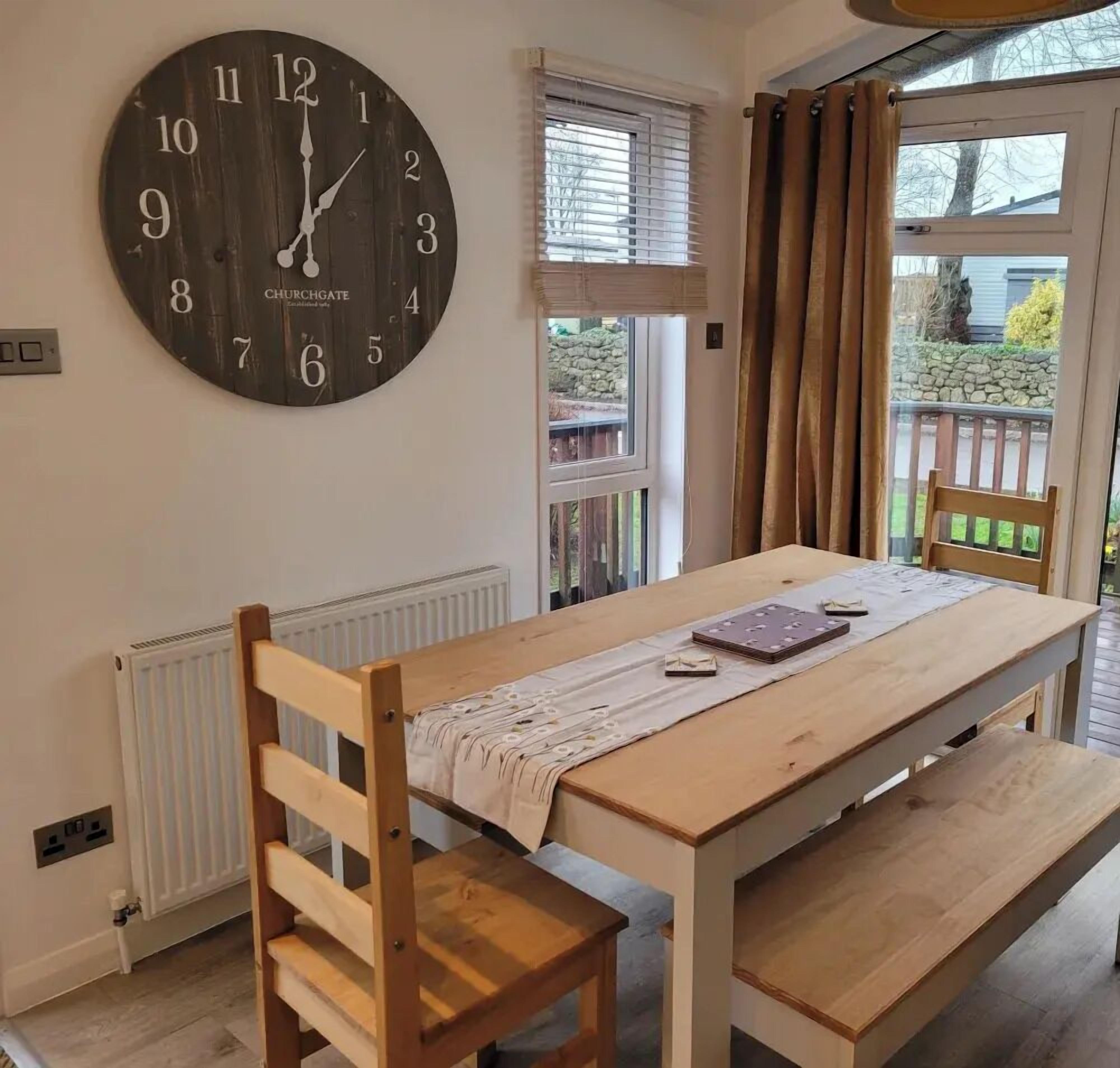 Un coin repas avec une table en bois, un banc et une horloge fixée au mur.