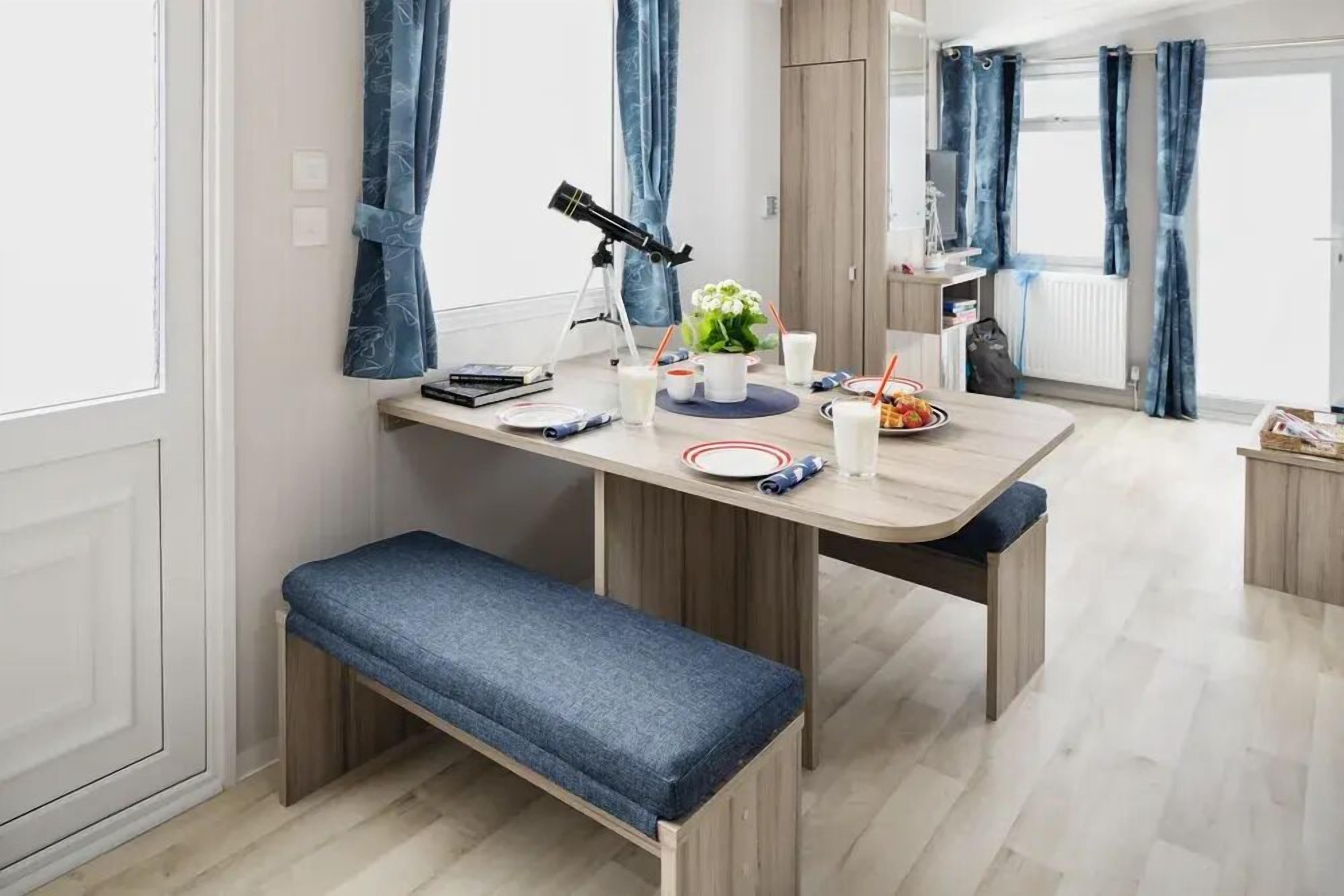 A modern dining area with a wooden table, benches, and a telescope.