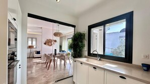 Una cocina moderna con armarios blancos, un ventanal grande y una zona de comedor con mesa y sillas.