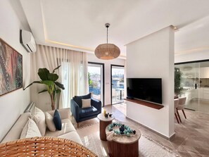 A modern living room with a sofa, a blue armchair, a TV, and a large window. - Sunny Andalouse S2 Apartment in Sidi Bou Saïd (Sidi Bou Said)
