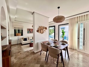 Uma sala de jantar com mesa posta para quatro pessoas, um sofá, um abajur e um objeto decorativo na parede.