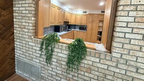 A kitchen with wooden cabinets, a microwave, and a window with hanging greenery. - Mega Mansion! 6BR-3.5BA | NYC | MetLife | Parking (Bayonne)