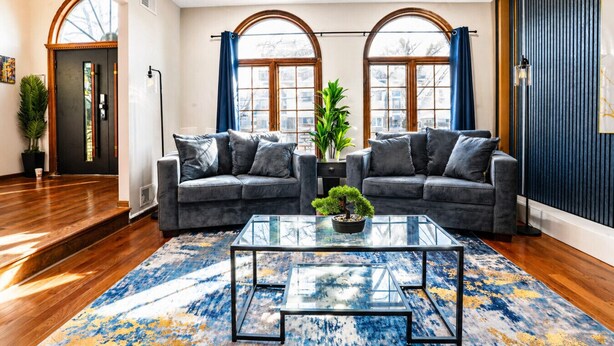 A living room with two sofas, a coffee table, and large windows with curtains. - Mega Mansion! 6BR-3.5BA | NYC | MetLife | Parking (Bayonne)