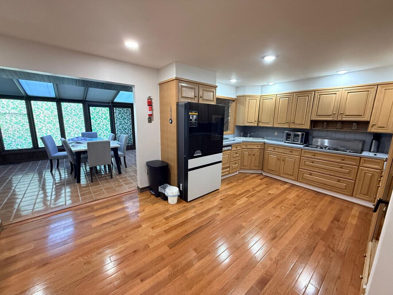 A modern kitchen with wooden cabinets, a refrigerator, and a dining area with a table and chairs.