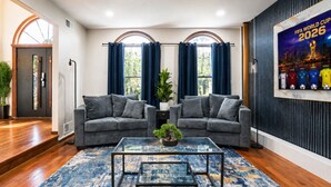 A modern living room with two grey sofas, a glass coffee table, and a blue patterned rug. - Mega Mansion! 6BR-3.5BA | NYC | MetLife | Parking (Bayonne)