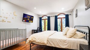 A bedroom with a bed, a desk, a chair, a crib, and a TV on the wall. - Mega Mansion! 6BR-3.5BA | NYC | MetLife | Parking (Bayonne)