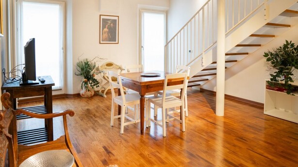 Uma área de refeições com uma mesa e cadeiras de madeira, uma escada e uma porta que dá para o exterior.