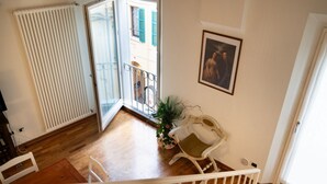 Quarto com piso de madeira, radiador branco, cadeira branca, planta em vaso e porta que dá para uma varanda externa.