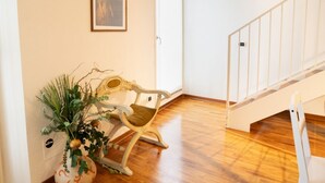 Quarto com piso de madeira, uma cadeira de balanço, corrimão branco e um quadro pendurado na parede.