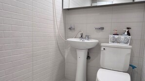Ein Badezimmer mit weißen Fliesen im U-Bahn-Stil, einem weißen Standwaschbecken, einer Toilette und einer Dusche mit Handbrause.