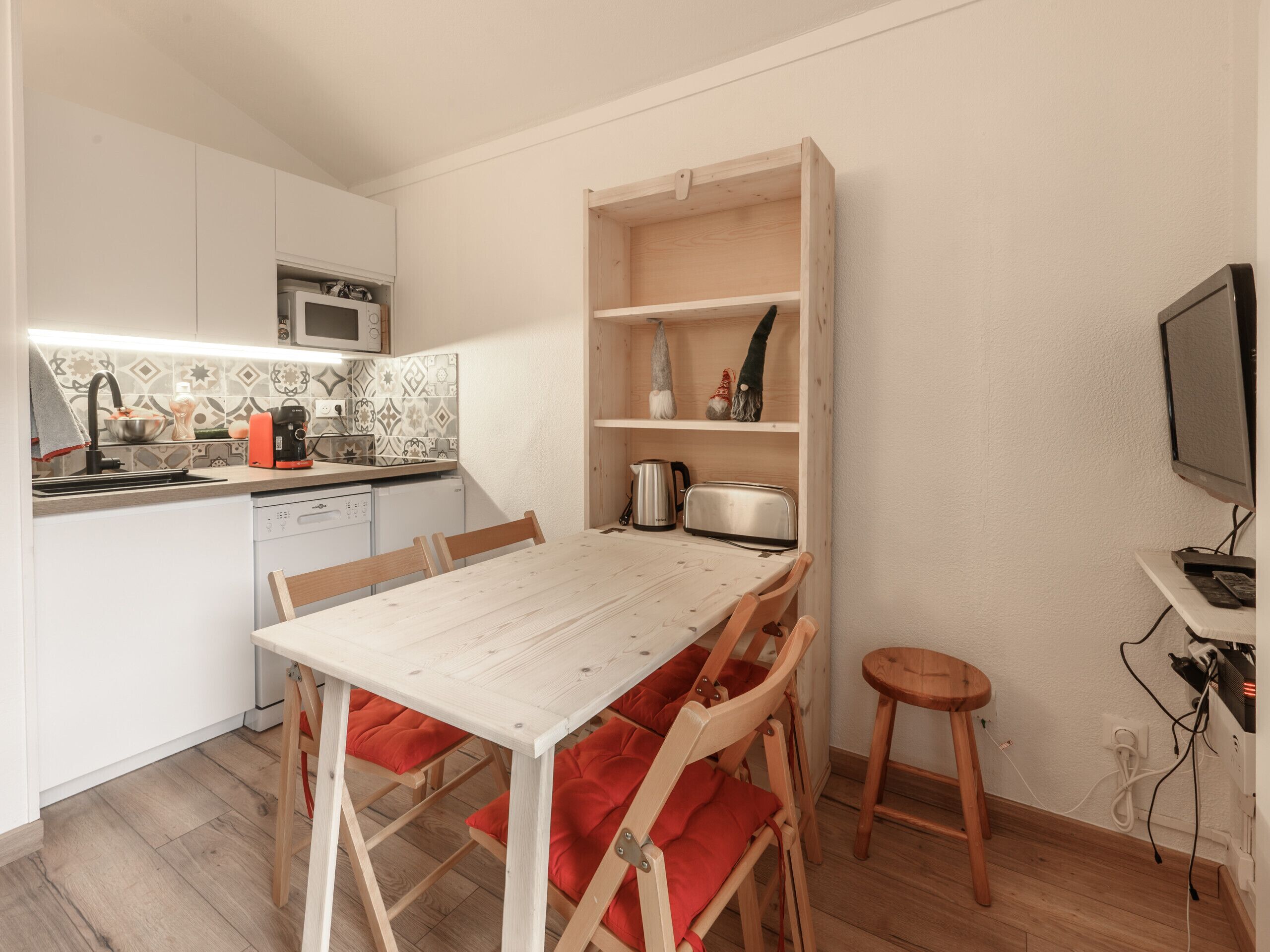 Une cuisine compacte comprenant une table à manger, des chaises, un four à micro-ondes, un évier et une petite étagère avec des objets décoratifs.