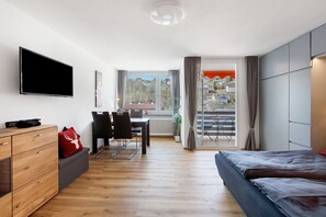 Ein modernes Hotelzimmer mit Flachbildfernseher, Essbereich, Schlafsofa und Blick auf die Stadt.