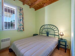 Een slaapkamer met een bed, een raam met gordijnen, een nachtkastje met een lamp en een radiator.