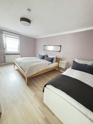 Une chambre avec deux lits, une fenêtre avec des stores, un radiateur et un miroir au mur.