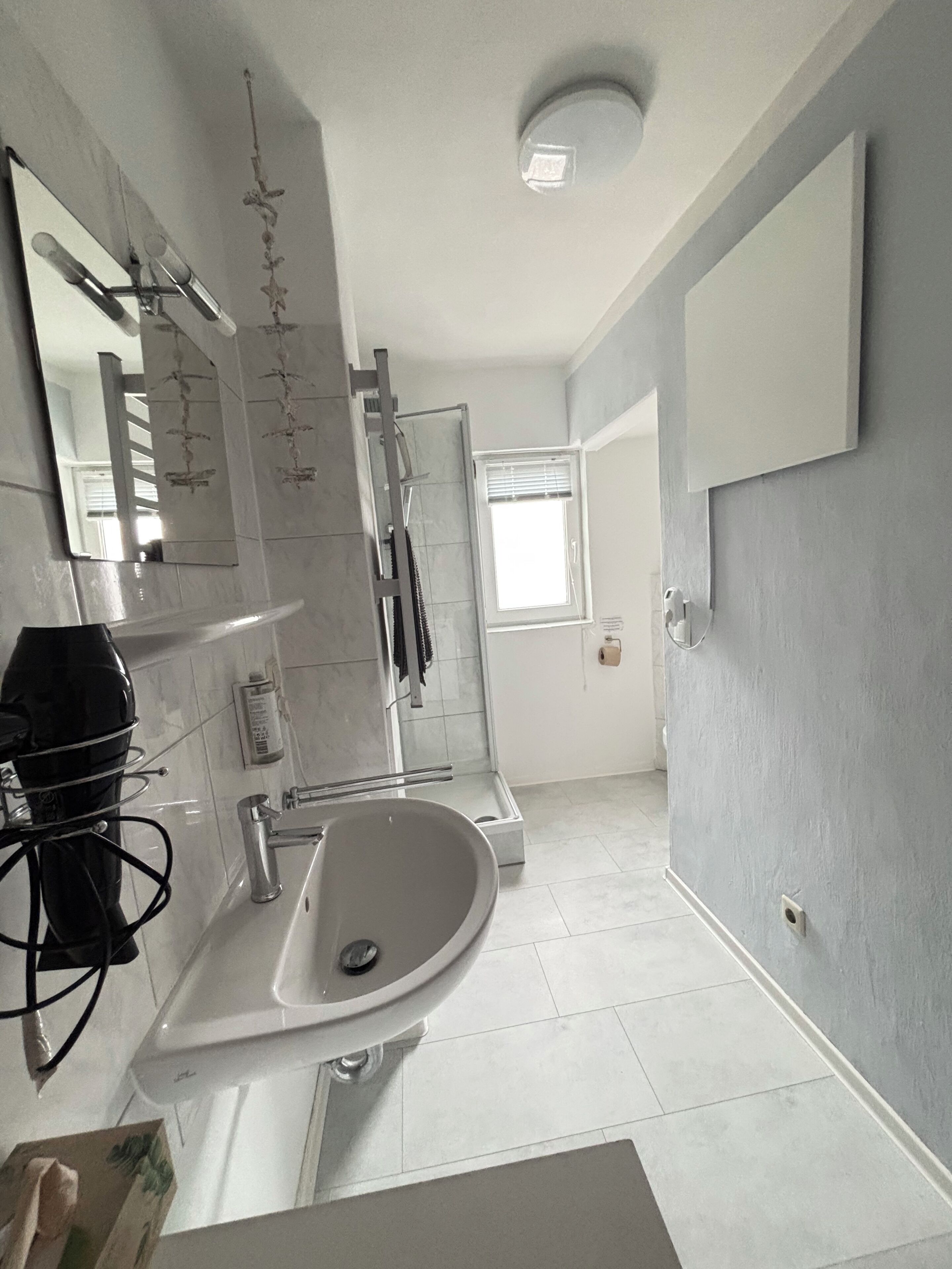 A bathroom with a sink, mirror, shower, and a window.