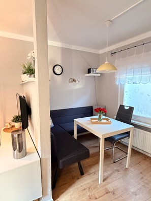 Un espace de vie moderne comprenant un canapé, une table à manger, une petite télévision, une horloge et une fenêtre donnant sur un beau paysage.