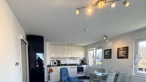 Ein modernes Wohnzimmer mit einem grünen Sofa, einem blauen Sessel und einem Essbereich mit Tisch und Stühlen.