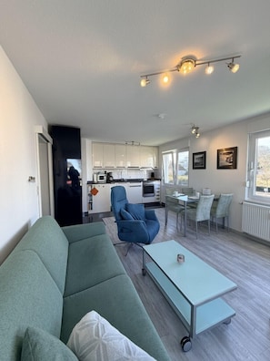Ein modernes Wohnzimmer mit einem grünen Sofa, einem blauen Sessel und einem Essbereich mit Tisch und Stühlen.