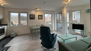 Eine moderne Wohnung mit Essbereich, Wohnzimmer mit Sofa, Fernseher und Küche mit Herd.
