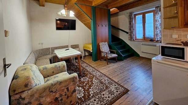 Een gezellige woonkamer met een bank, een tafel, een televisie en een trap die leidt naar een keuken met een magnetron.
