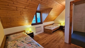 Een slaapkamer met een schuine kap, twee bedden, een radiator en een raam.