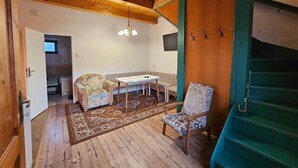 Een gezellige kamer met houten balken, een eettafel, twee stoelen, een kamerbreed tapijt en een trap.