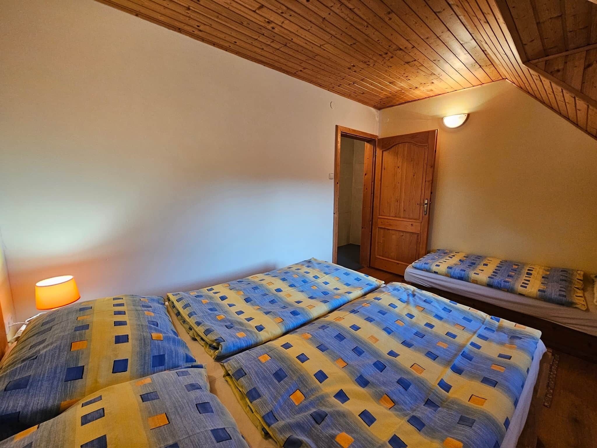 A room with two beds, a wooden ceiling, a door, and a wall-mounted light.