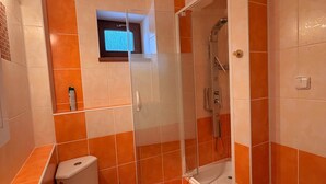A bathroom with orange tiles, a glass shower enclosure, a toilet, and a sink.
