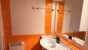 A bathroom with orange and white tiles, a white sink, a mirror, and a towel rack.