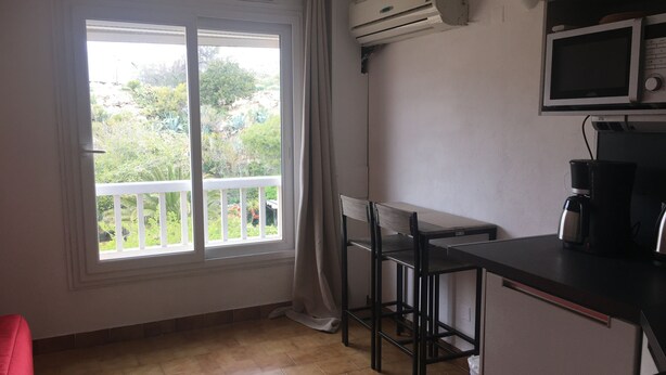 Une pièce avec une grande fenêtre, une kitchenette équipée d’un four à micro-ondes et un fauteuil rouge.