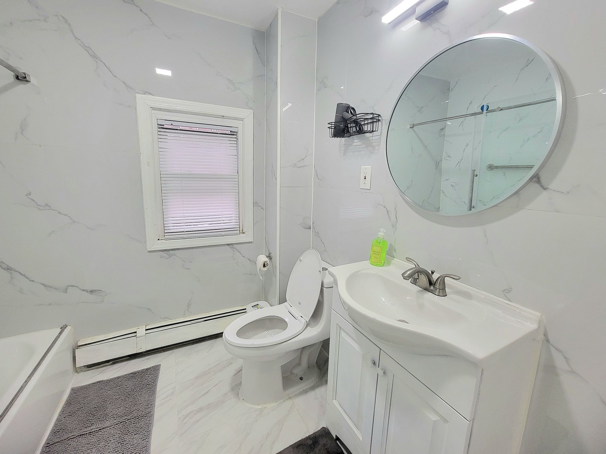 A bathroom with a toilet, sink, mirror, and window.