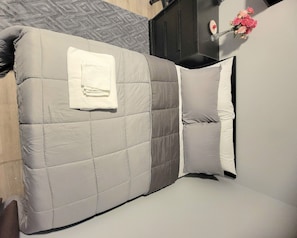 En säng med ett vadderat sänggavel, en vikt hopfälld vit handduk och en vas med blommor på nattduksbordet.