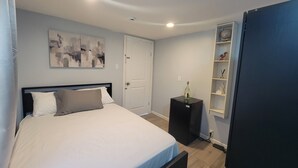Ein Schlafzimmer mit einem Bett, einer weißen Tür, einem schwarzen Schrank und einem Regal mit Dekoration.