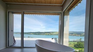A modern bathroom with a freestanding bathtub, large sliding glass doors, and a view of a lake and hills.