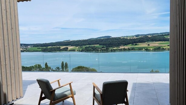 A balcony with two chairs and a view of a lake and hills.