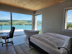 A bedroom with a bed, a desk, and a large bathtub. - Lakeview Guest Rooms Rooftop Terrace (Ebikon)