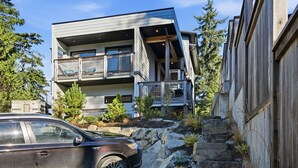 A modern multi-story building with a balcony, surrounded by trees and rocks.