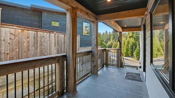A covered outdoor area with a wooden deck, a metal railing, and a view of a forest.