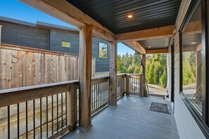 Un espace extérieur abrité, doté d’une terrasse en bois, d’une rambarde en métal et offrant une vue sur une forêt.