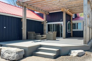 A covered outdoor area with a wooden pergola, a set of steps leading to a door, and wicker furniture.