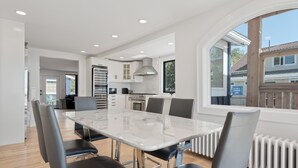 A modern kitchen with white cabinets, a large island, and a view through a window.