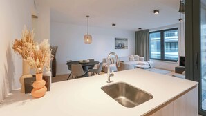 Una cucina moderna con isola centrale, lavello in acciaio inossidabile e zona pranzo con tavolo e sedie.