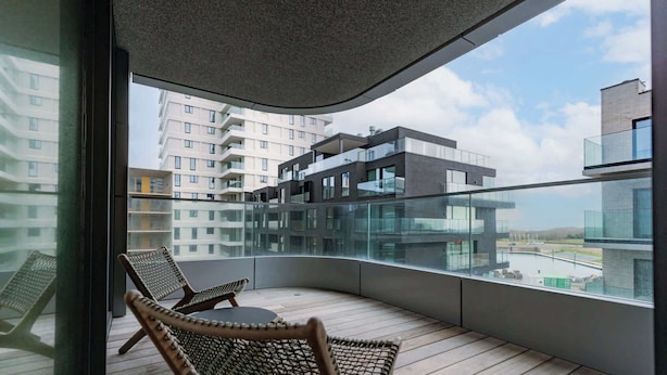 Un balcone con sedie in vimini, ringhiera in vetro e vista su edifici moderni.