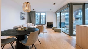 Un soggiorno moderno con un tavolo da pranzo in legno scuro, sedie imbottite grigie, un divano e un'ampia finestra con vista sugli edifici.