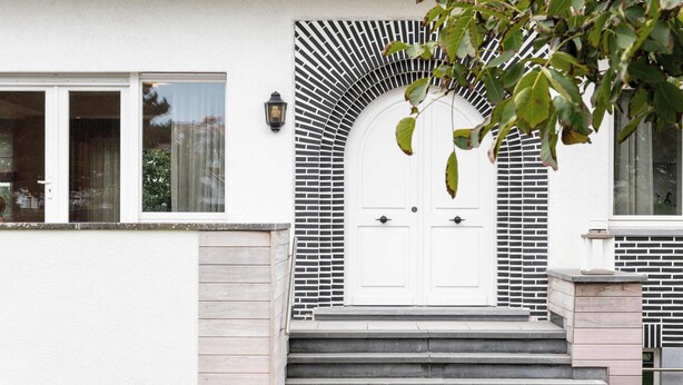 A white building with a white door, black and white patterned wall, and a set of stairs leading to the entrance.
