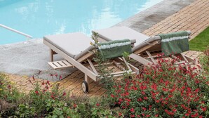 A poolside area with two lounge chairs, a small cart, and a garden with red flowers.