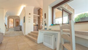 A spacious living area with a staircase leading to a kitchen, a dining area with a wooden table, and a view of the outdoors. - Calypso Lux Independent Villa (AGLIENTU)