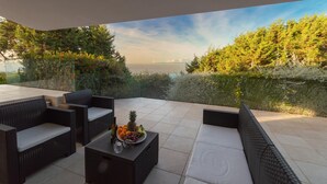 A patio with wicker furniture, a table with fruit, and a view of the sea and trees. - Calypso Lux Independent Villa (AGLIENTU)